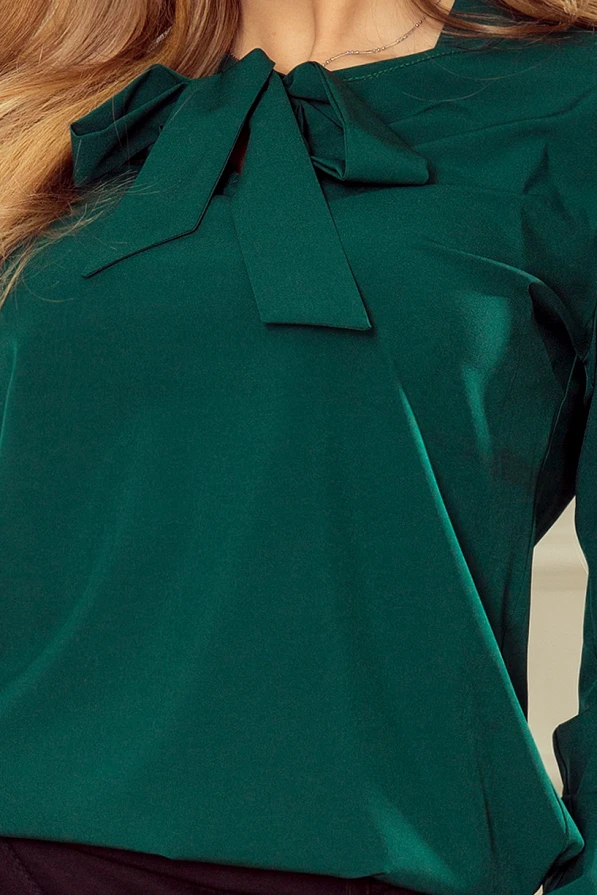 A stylish green blouse featuring an elegant bow tie detail at the neckline. The fabric has a smooth, slightly shiny finish, adding a touch of sophistication.