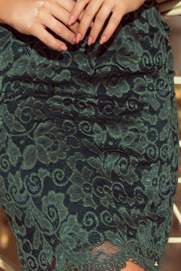 The image features a close-up of an elegant lace dress in a deep green hue, showcasing intricate floral patterns. The fabric has a delicate, textured appearance, adding a touch of sophistication and charm.