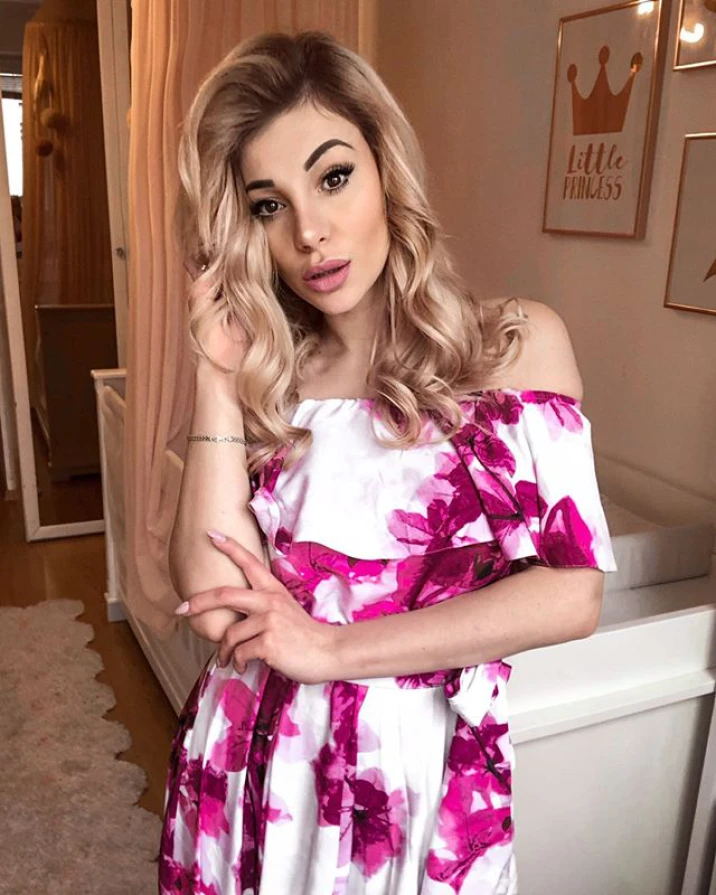 A long, elegant dress with an off-the-shoulder design features a vibrant pink floral pattern on a white background. The flowing fabric and feminine silhouette make it perfect for special occasions.
