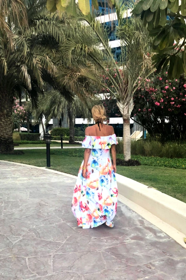 A long, flowing summer dress with a vibrant floral pattern, featuring an off-the-shoulder design perfect for warm weather. The dress exudes a breezy elegance, ideal for a casual stroll or a beach outing.