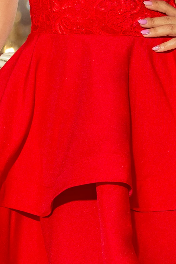 A vibrant red dress features a double flared skirt with intricate lace detailing on the bodice. The elegant design is complemented by a layered hem, adding a touch of sophistication.