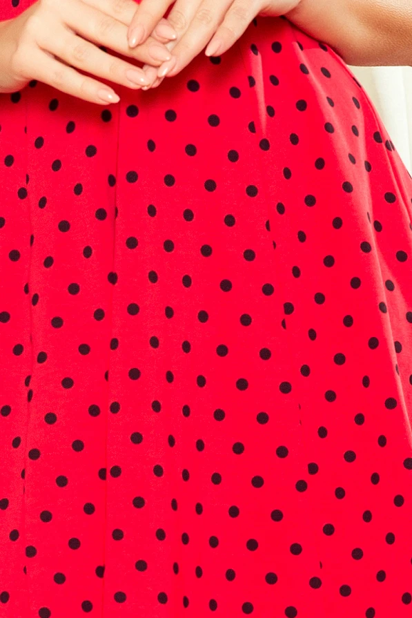 A vibrant red dress with a flared skirt features a playful black polka dot pattern. The fabric appears smooth and lightweight, perfect for a lively and stylish look.