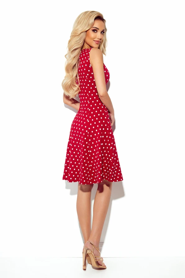 A woman is wearing a red, sleeveless dress adorned with white polka dots, featuring a flared skirt that adds a playful touch. The dress is paired with nude high-heeled sandals, creating an elegant and stylish look.