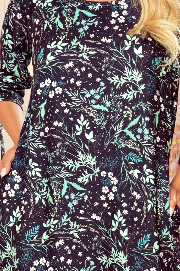 The dress features a comfortable, loose fit with a vibrant floral pattern in shades of green and white on a dark background. Its design includes long sleeves and a round neckline, perfect for a casual yet stylish look.