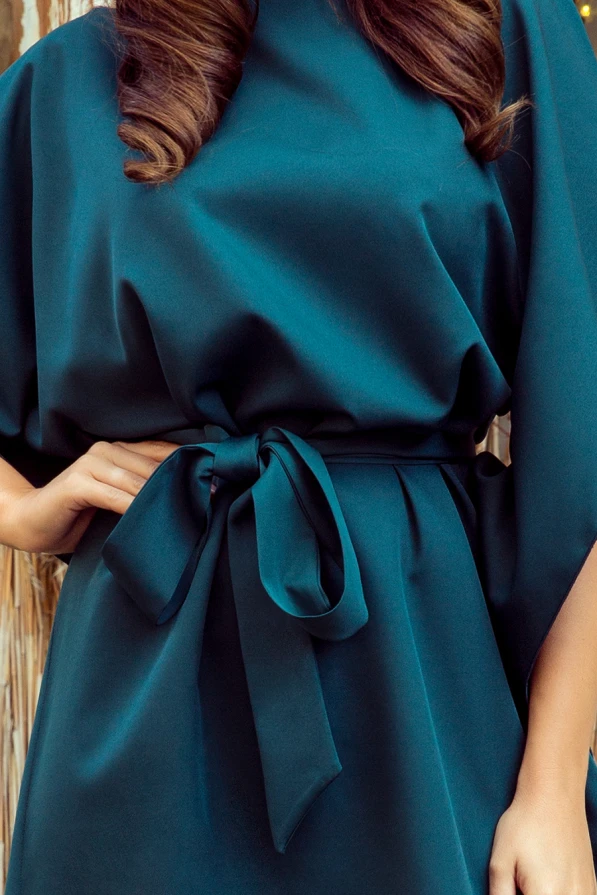 The image showcases an elegant green dress with a smooth, flowing fabric and a stylish waist tie. The dress features a sophisticated design, perfect for formal occasions.