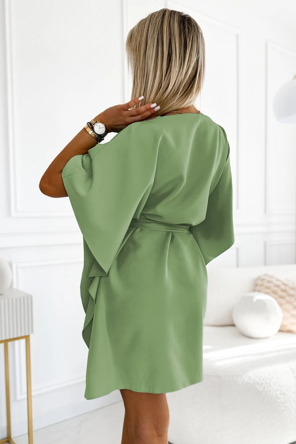 A woman is wearing a light green, short-sleeved dress with a loose, flowing fit and a belt at the waist. The dress has a soft, elegant drape, perfect for a casual yet stylish look.