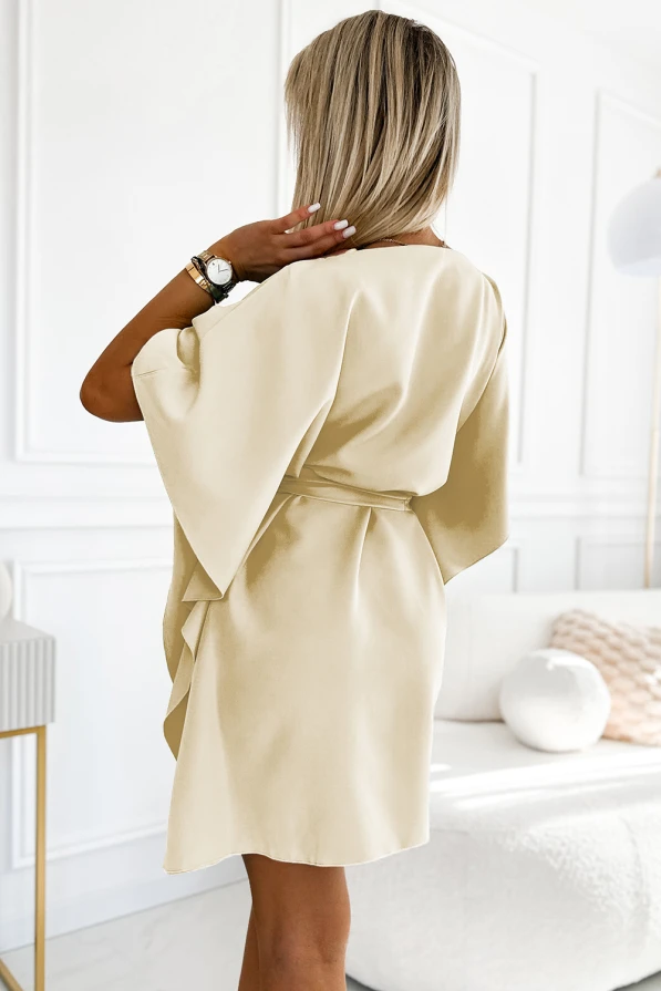 A woman is wearing a light beige, short-sleeved dress with a loose fit and a belt at the waist. The dress has a soft, flowing fabric that drapes elegantly, perfect for a chic and comfortable look.