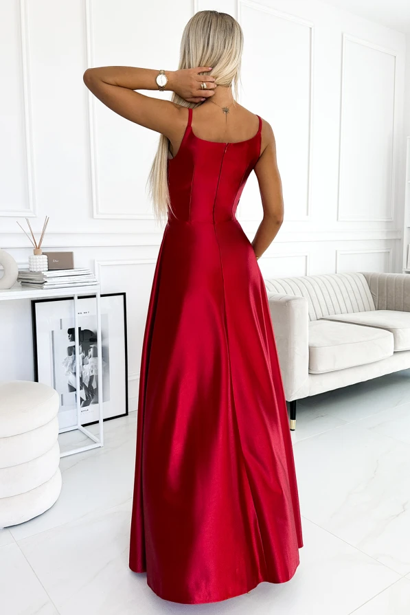 A woman is wearing an elegant, floor-length red maxi dress with thin straps, showcasing a sleek and sophisticated design. The dress has a smooth, flowing fabric that drapes beautifully, perfect for formal occasions.