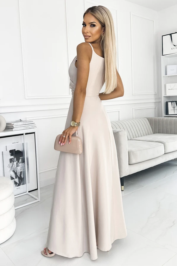 A woman is wearing an elegant, sleeveless maxi dress in a soft beige color, perfect for formal occasions. She holds a matching clutch, complementing the dress's sophisticated and timeless design.