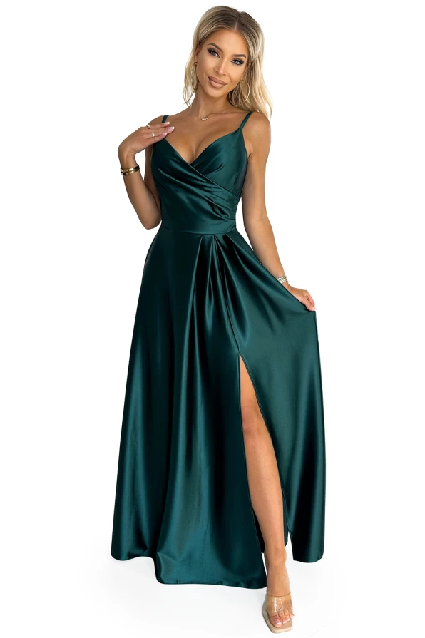 A woman is wearing an elegant, deep green satin maxi dress with a fitted bodice and a flowing skirt featuring a high slit. The dress has thin straps and a draped neckline, adding a touch of sophistication.
