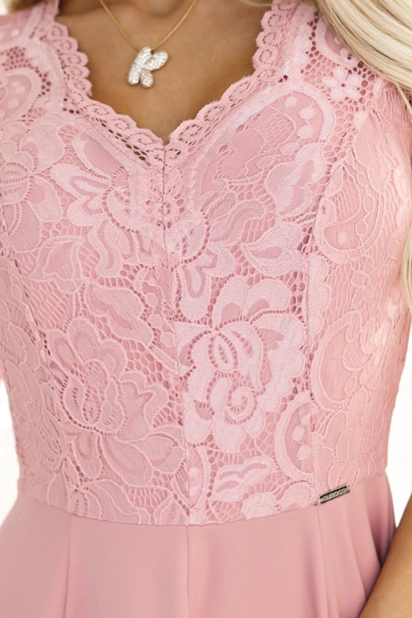 A close-up of an elegant long dress in a soft pink hue, featuring intricate lace detailing on the bodice. The dress is complemented by a delicate necklace with a butterfly pendant.