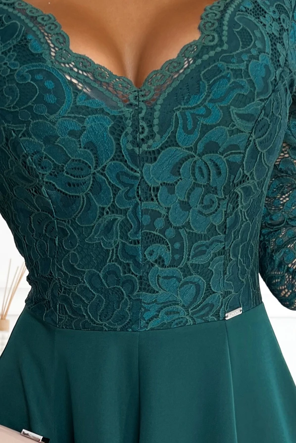 The image showcases an elegant dress featuring a deep green lace bodice with intricate floral patterns. The design is complemented by a smooth, flowing skirt, creating a sophisticated and stylish look.