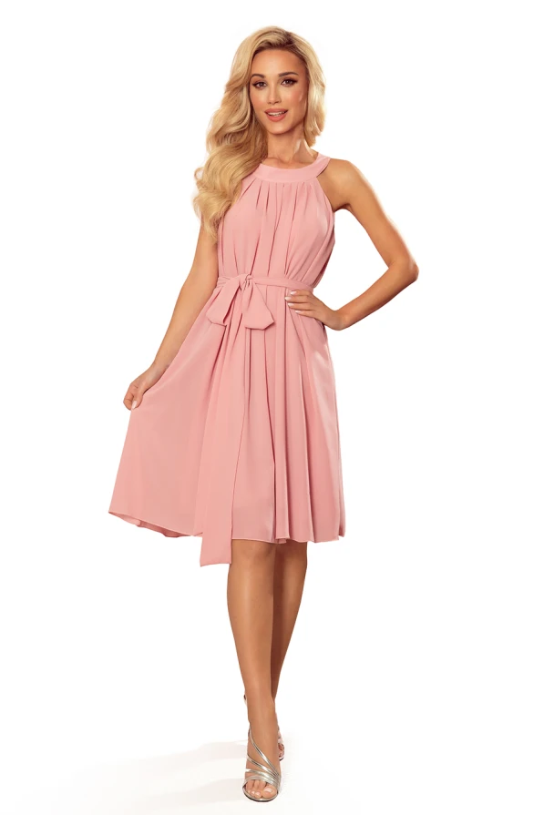 A light pink chiffon dress with a halter neckline and a flowing, knee-length skirt is elegantly designed with a tied waist detail. The dress exudes a soft, feminine charm, perfect for both casual and formal occasions.