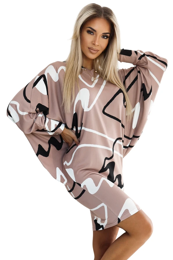A stylish, oversized sweater dress featuring an abstract black and white pattern on a soft, beige background. The dress has long, flowing sleeves and a relaxed fit, perfect for a comfortable yet fashionable look.