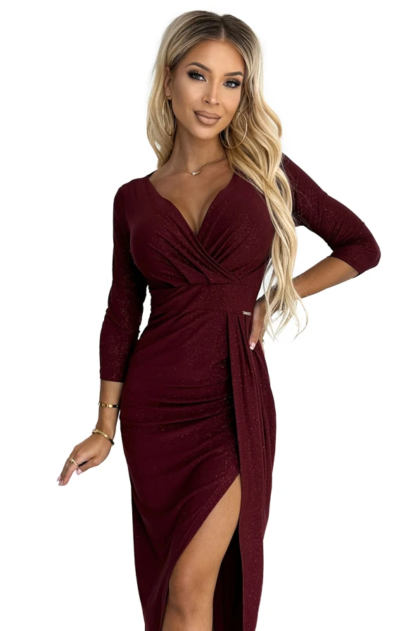 A shimmering burgundy dress with a deep V-neckline and three-quarter sleeves, featuring a gathered waist and a stylish side slit. The fabric has a subtle sparkle, adding elegance and sophistication to the overall look.