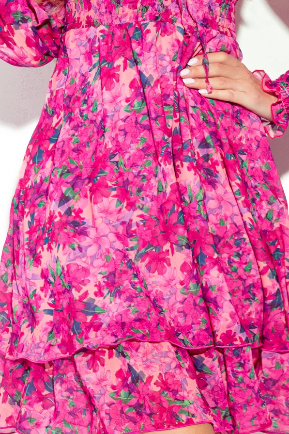A vibrant chiffon dress adorned with a lively floral pattern in shades of pink and green. The dress features a flowing, layered design with delicate ruffle details on the sleeves and hem.