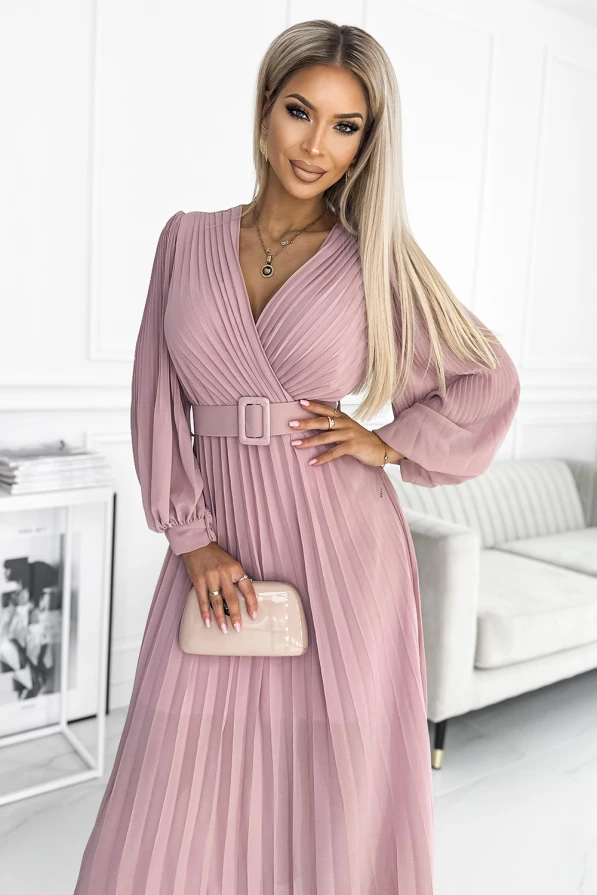 A pleated, long-sleeve dress in a soft pink hue features a wrap-style bodice and a matching belt that accentuates the waist. The elegant design is complemented by a glossy nude clutch, adding a touch of sophistication.