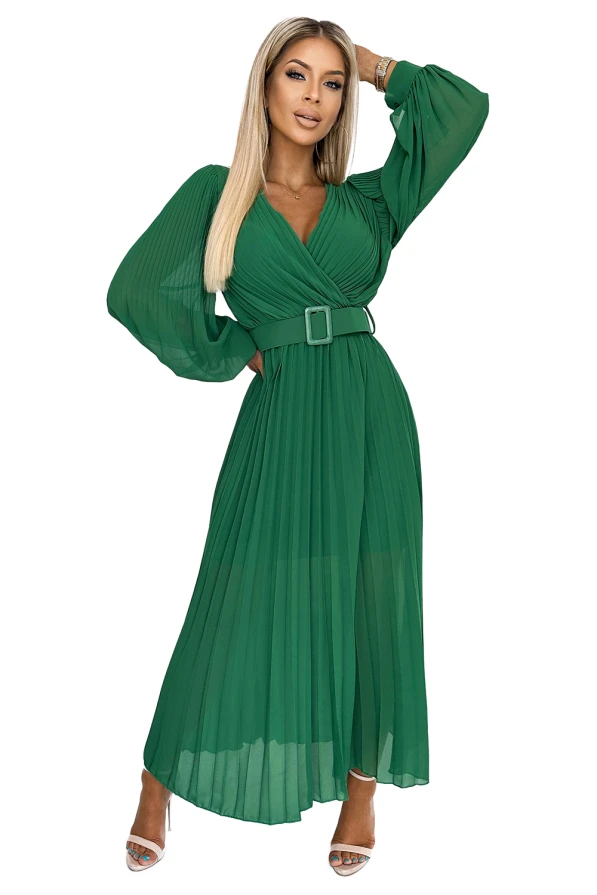 A green pleated dress with long, flowing sleeves and a matching belt accentuates the waist. The dress features a deep V-neckline and a graceful, elegant silhouette.
