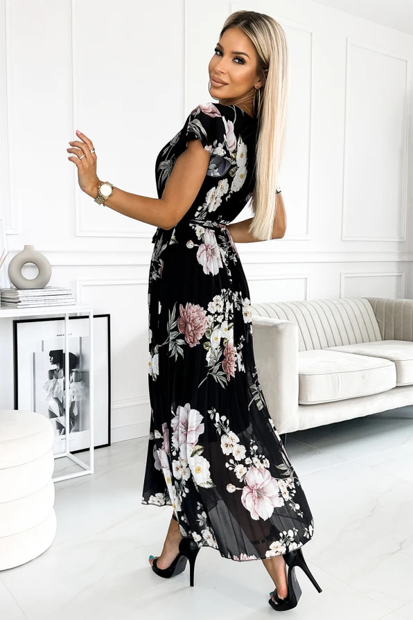A pleated dress with a floral pattern in shades of pink and white on a black background, featuring short sleeves and a flowing, elegant silhouette. The dress is styled with high heels, creating a sophisticated and chic look.
