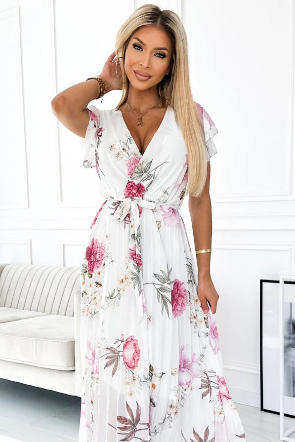 A flowing, pleated dress with a floral pattern in shades of pink and green on a white background. The dress features a V-neckline and short, flutter sleeves, complemented by a tied waist for a flattering silhouette.