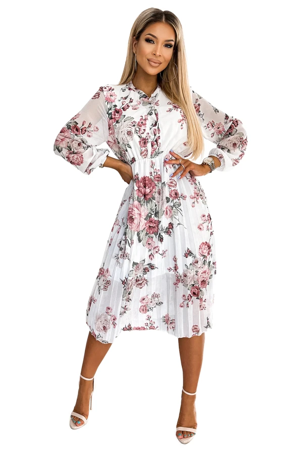 A pleated dress with a floral pattern featuring shades of pink and green on a white background. The dress has long sleeves and a button-up front, offering a stylish and elegant look.