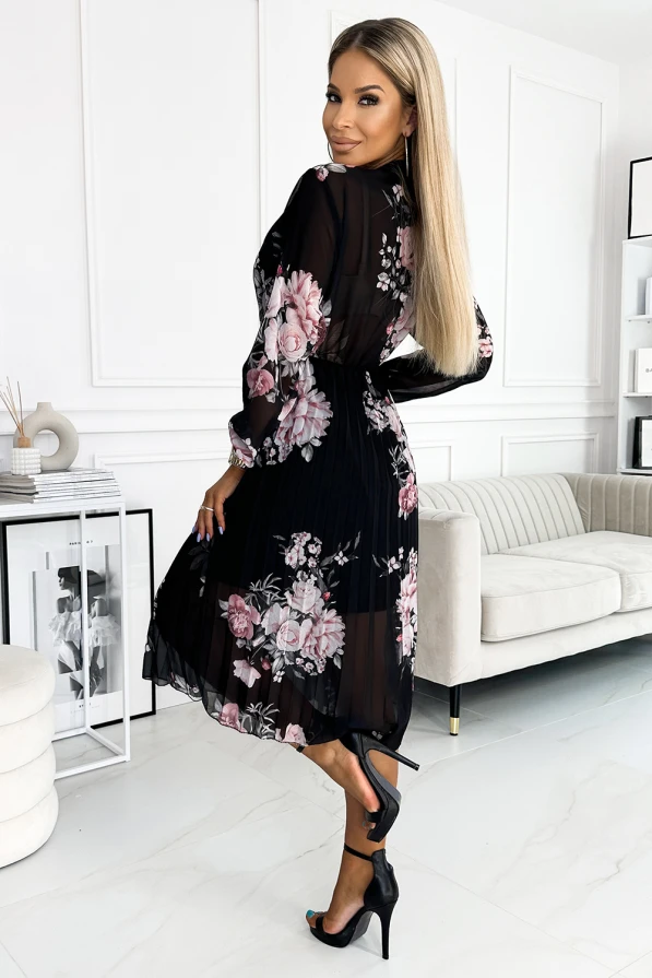 A black pleated dress adorned with pink floral patterns, featuring long sleeves and a flowing, elegant silhouette. The sheer fabric adds a touch of sophistication, making it perfect for both formal and casual occasions.