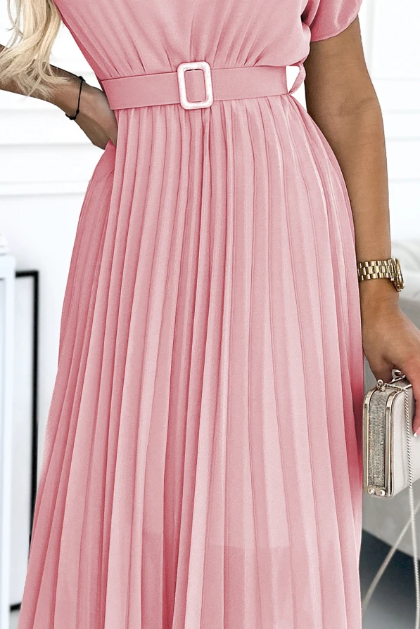 A pink pleated dress with a matching belt and a square buckle, featuring short sleeves and a flowing skirt. The outfit is accessorized with a gold watch and a small metallic clutch.