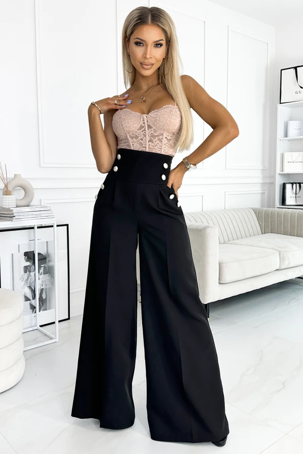 A stylish woman is wearing elegant wide-leg black trousers with decorative buttons at the waist. The trousers are paired with a delicate lace top, creating a sophisticated and chic look.