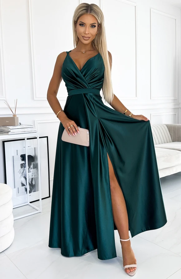 A long, elegant satin dress in a deep emerald green features a flattering V-neckline and a high slit for added sophistication. The dress is complemented by a matching clutch, creating a chic and polished look.