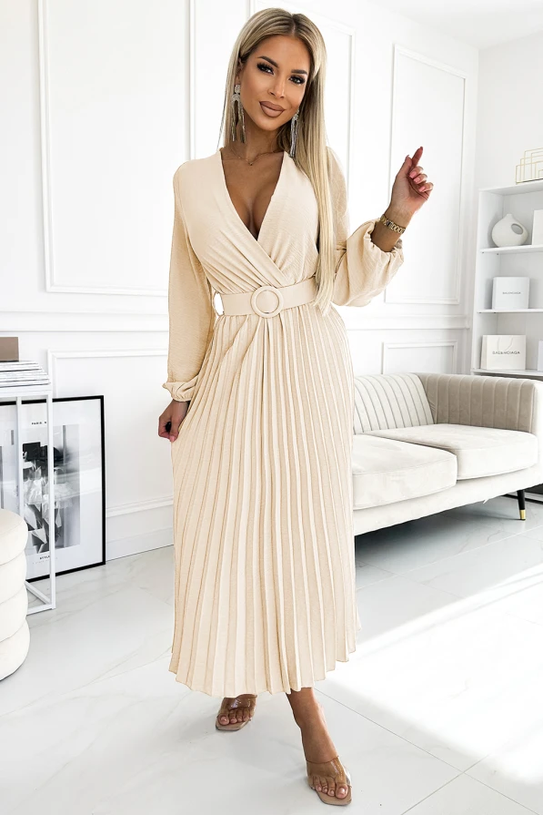 A beige pleated dress with long sleeves and a stylish belt featuring a circular buckle, creating an elegant and sophisticated look. The dress is perfect for formal occasions, offering a blend of classic design and modern flair.