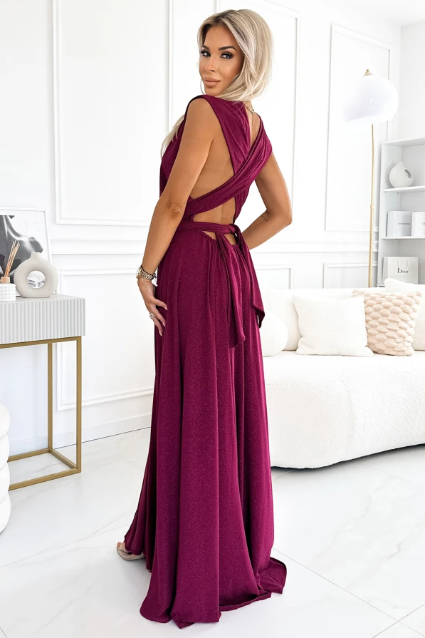 A long, elegant dress in a rich burgundy color features a flowing skirt and a stylish open back with crisscross straps. The design is sophisticated, perfect for formal occasions, and adds a touch of glamour to any wardrobe.
