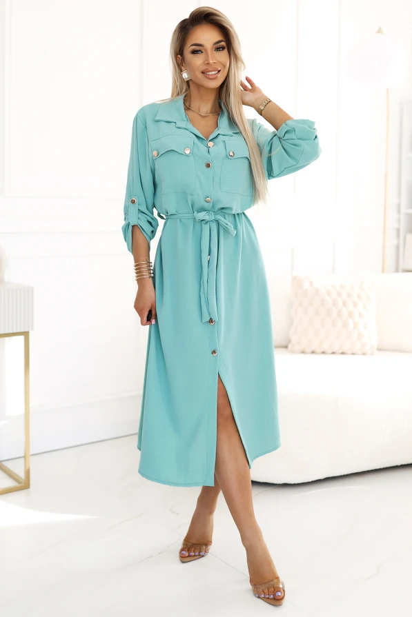 A stylish midi shirt dress in a soft turquoise color features a button-down front and a matching waist tie for a flattering silhouette. The dress is complemented by rolled-up sleeves with button tabs and subtle gold accents on the buttons.