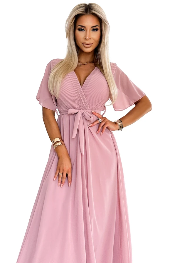 A long, elegant dress in a soft pink hue features delicate pleats and a flattering V-neckline. The dress is complemented by short, flowing sleeves and a waist tie, adding a touch of sophistication.